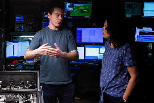 Man and woman in discussion near multiple computer monitors