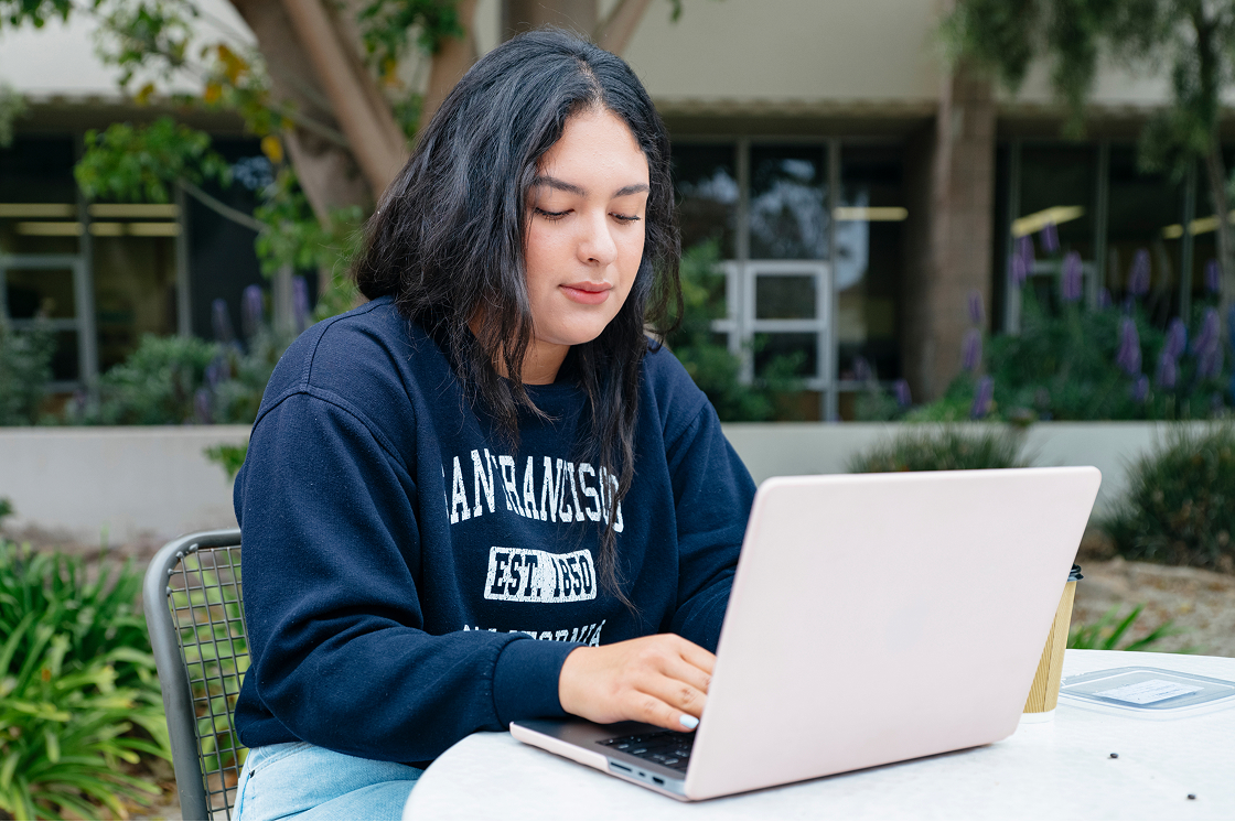 Woman in UCSB sweatshirt seated outside working on laptop